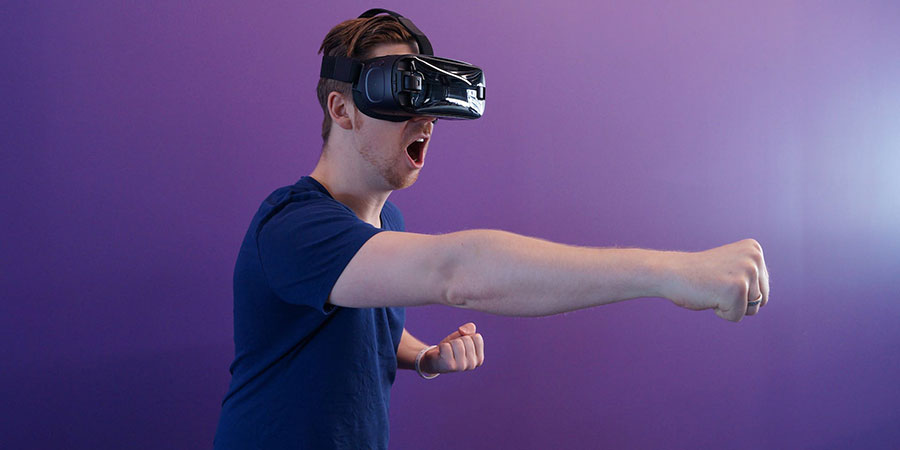 man wearing navy blue t-shirt, punching in the air while wearing VR goggles
